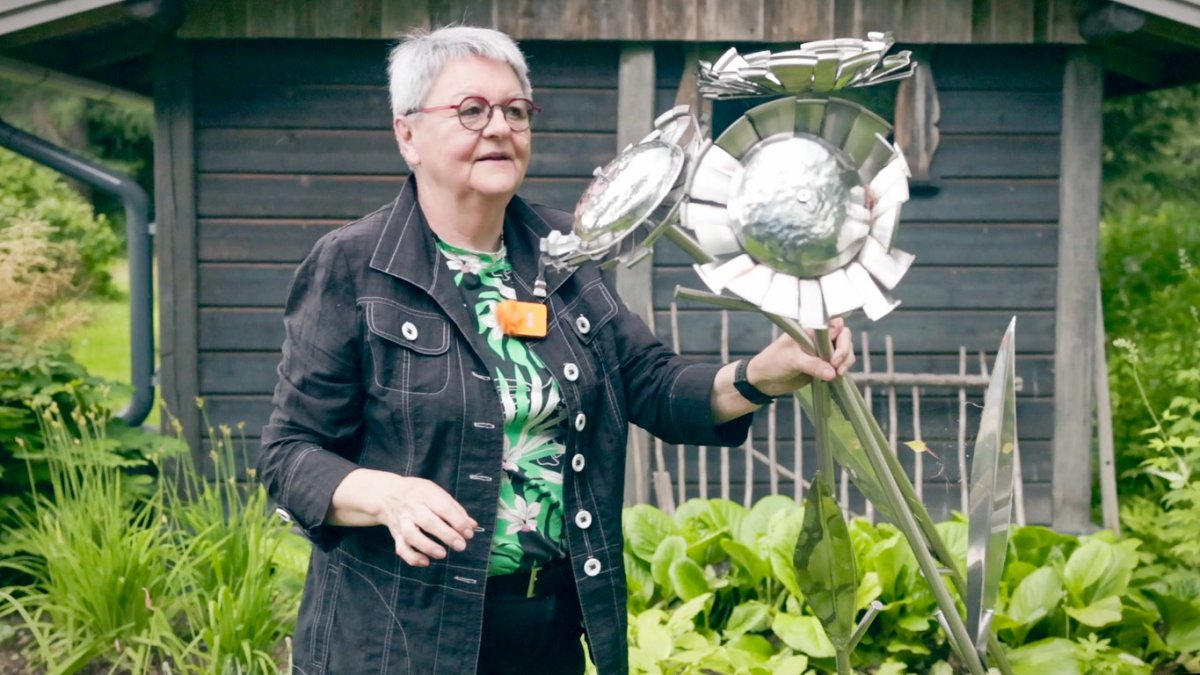 Liisa esittelemässä itse tekemäänsä teostaan kesäisessä maisemassa 